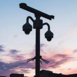 Silhouette of security cameras against a vibrant sunset sky, showcasing modern surveillance technology.